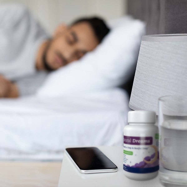 Man sleeping in bed with Natural Dreams, water, and his phone on the nightstand